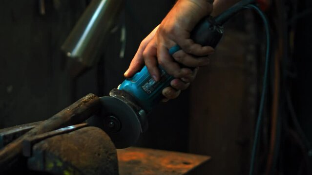 hands hold grinder in dark workshop and cut steel pipes with yellow sparks