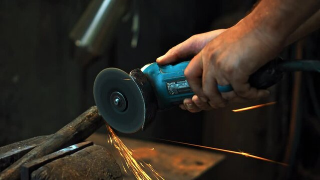 hands hold grinder in dark workshop and cut steel pipes with yellow sparks