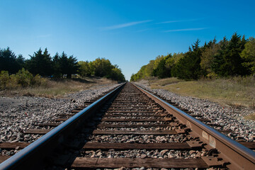 A set of railroad tracks disappearing on the distant horizon as they head over a small tree lined...