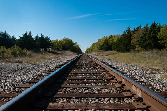 A set of railroad tracks disappearing on the distant horizon as they head over a small tree lined hill on a sunny morning.
