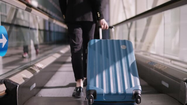 Passenger with suitcase confidently navigate the airport with blue rolling suitcase, female torist moving with luggage on  terminal walkway portraying efficiency and rhythm of contemporary travel.
