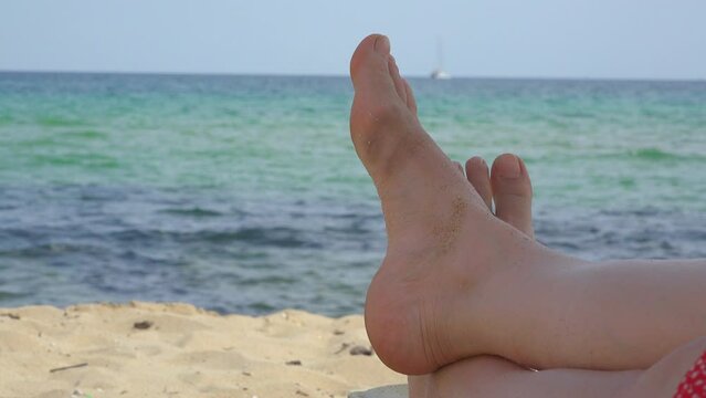 Barefoot woman feet detail on beach, sea in background