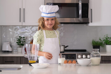 Fototapeta na wymiar Child in chef hat and apron preparing food in the kitchen. Cooking children. Child boy with apron and chef hat preparing a healthy meal in the kitchen. Cooking process.