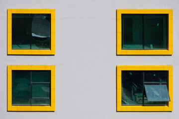 Four windows with yellow frames in a white color wall. Exterior of a building with yellow frame windows.
