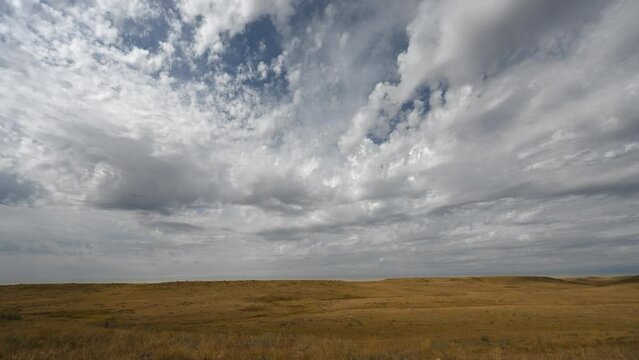 Time lapse of spectacular puffy white summer clouds moving towards the viewer over a dry prairie setting. Sunlight moves across the dry grass highlighting the small hills.
