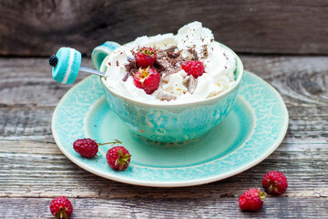 A beautiful blue cup of coffee with whipped cream, cocoa powder and raspberries on rustic wooden background