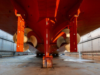 Ship in dry dock. Bronze twin propeller and rudder, red hull. 




