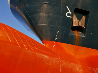 Ship bulbous bow out of water in dry dock. Draft marks on hull. Anchor and rust.