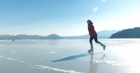 Tapeten LENS FLARE: Cheerful young woman enjoys ice skating on a naturally frozen lake © helivideo