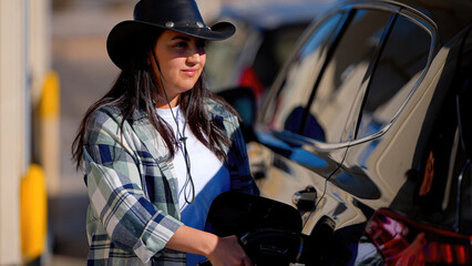A fierce cowgirl at a gas station, her hat and clothing exuding western charm, she fills up with...