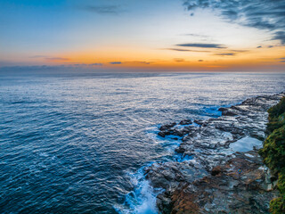 Obraz premium Sunrise over the calm ocean with light cloud and rocks
