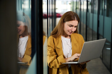 Beautiful woman stands with laptop in corridor of coworking space