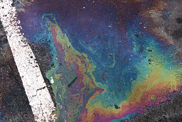 Oil spill on wet asphalt, parking lot with dividing line.