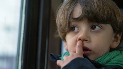 Close-up face of small boy nose picking. Introspective kid traveling by train