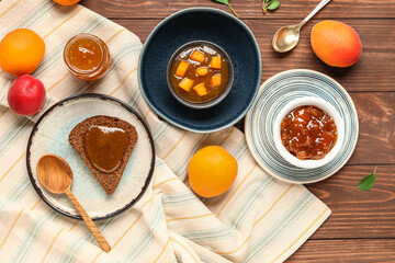 Bowls with sweet apricot jam and toast on wooden background