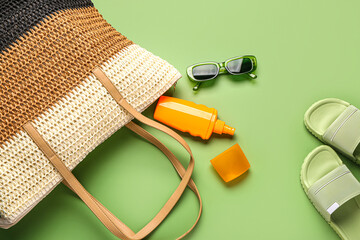 Bottle of sunscreen cream with wicker bag and sunglasses on green background