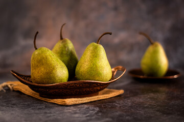 A group of ripe pears arranged on a decorative bronze tray, placed on a dark surface with a hazy...
