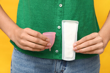 Beautiful young woman with menstrual cup and pad on yellow background