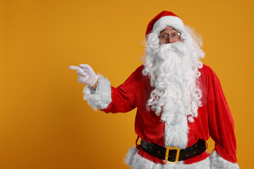 Fototapeta na wymiar Merry Christmas. Santa Claus pointing at something on orange background, space for text