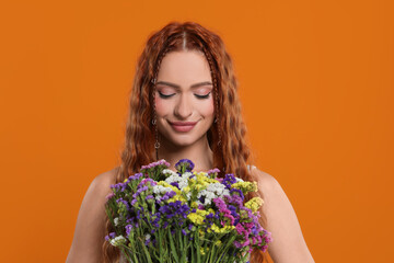 Beautiful young hippie woman with bouquet of colorful flowers on orange background