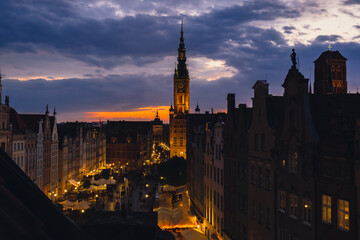 Fototapeta premium Beautiful old town in Gdansk at summer dusk Poland. Sunset night view from the window rooftop on historical centre Dluga street and city hall architecture buildings St Mary Basilica. Travel attraction