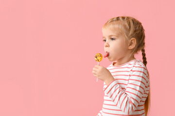 Cute little girl eating sweet lollipop on pink background