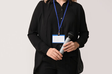 Female journalist with microphone and blank ID badge on grey background, closeup