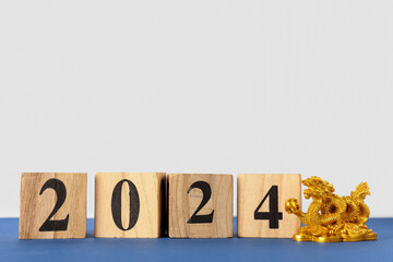 Golden dragon figurine and wooden cubes with figure 2024 on blue table against white background....