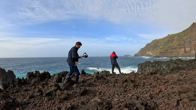 Two photographer taking pictures of the rough sea and the cliff while the waves break in Azores in a sunny day
