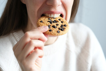 Close up an unrecognizable woman bite bite of healthy muesli cookie, traditional and popular...