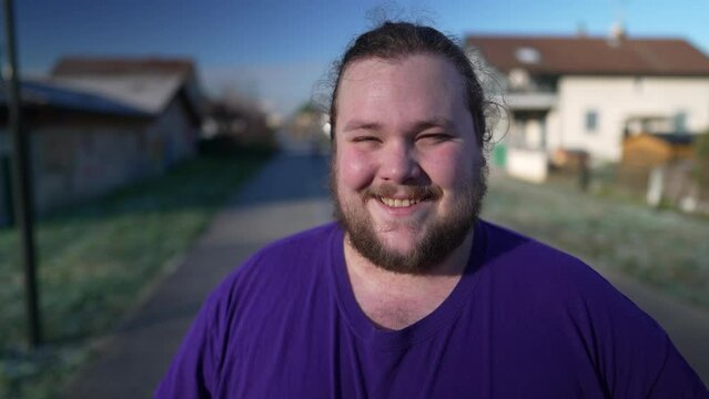 Portrait of a happy overweight young man standing outside smiling at camera. One chubby male caucasian casual person