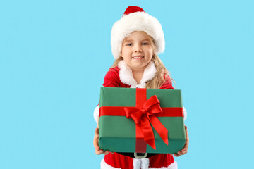 Cute little girl in Santa Claus costume with Christmas gift on blue background
