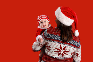 Cute little baby in Santa Claus costume with mother on red background