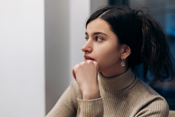 Young pretty confident woman sitting inside cafe waiting for order, thinking about something
