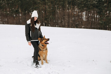 Young woman walk the dog German Shepherd in winter field forest, running playing with snow, training the animal in harsh conditions, wind blowing. Christmas Time, New Year
