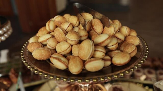 Close up pile of baked sweet cookies at nuts shape filled boiled condensed milk, caramel or cream on golden plate on candy bar at restaurant. Eastern Europe traditional homemade crunchy pastry.
