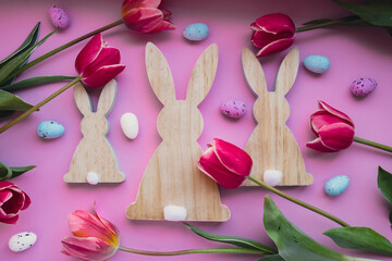 Easter eggs and wooden bunnies with pink tulips on violet pastel background. Flat lay composition, top view. Decoration minimalist modern design template. Floral layout Concept of creative 