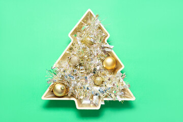 Plate in shape of Christmas tree with tinsel and balls on color background