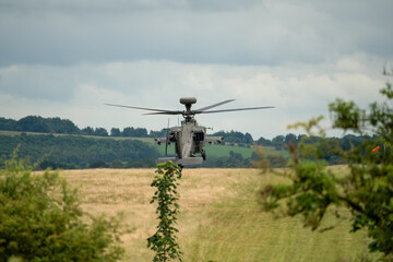Fototapeta na wymiar British army Boeing Apache Attack helicopter gunship AH64E (AH-64E Army Air606) hovering low over summer countryside