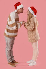 Happy young couple in Santa hats kissing on pink background