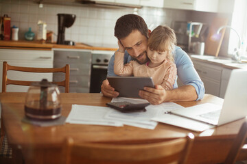 Father and daughter sitting at desk with documents using tablet at home
