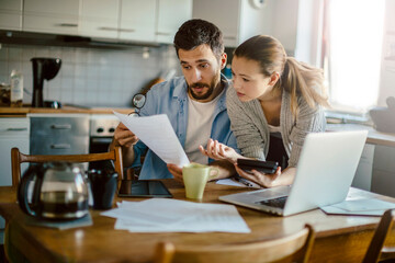 Young couple reading bad financial report having financial debt at home - obrazy, fototapety, plakaty