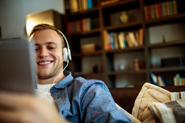 Close up smiling young man with headphones holding smartphone at home