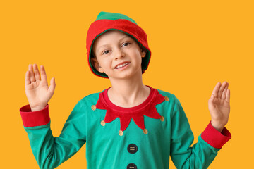 Cute little boy in elf's costume waving hands on yellow background