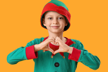 Cute little boy in elf's costume showing heart gesture on yellow background