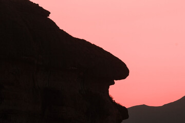 silhouette of a rock; silhouette of a baboon face from 
 a rock against evening light;...