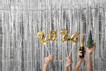Female hands with champagne bottle and figure 2024 made of balloons on silver tinsel background