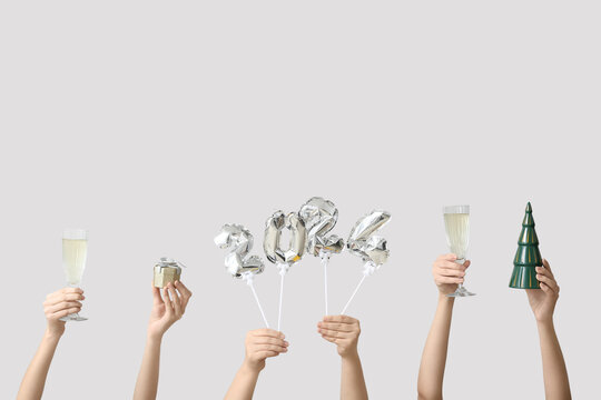 Female hands with figure 2024 made of balloons and glasses of champagne on white background