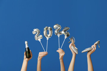 Female hands with champagne bottle, high heel shoes and figure 2024 made of balloons on blue...