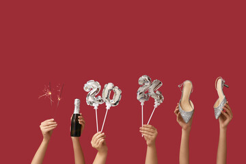 Female hands with high heel shoes, champagne bottle and figure 2024 made of balloons on red...